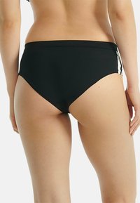 Bas de bikini noir taille haute avec accents blancs sur les côtés, texture lisse et coupe ajustée. Offre une couverture minimale à l'arrière.