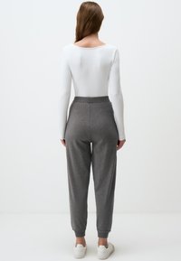 Graue, schmal zulaufende Sweatpants mit einem gerippten Bund, kombiniert mit einem weißen Langarmoberteil. Der Stoff wirkt weich und strukturiert.