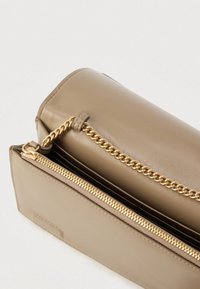 Τσάντα χειρός σε ταμπά δέρμα με γυαλιστερό φινίρισμα, διακόσμηση με χρυσή αλυσίδα, κλείσιμο με φερμουάρ και στρογγυλεμένο σχήμα. Ορατές υφασμάτινες λεπτομέρειες στο εσωτερικό.