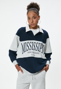 Pullover in cotone navy e grigio con collo a camicia, con la scritta "MISSISSIPPI NEW ORLEANS U.S.A." in grassetto sulla parte anteriore.