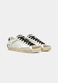 Sneaker bianchi con accenti in suede grigi e marroni, lacci neri e una suola testurizzata. Presentano dettagli di cucitura e un marchio sul lato.