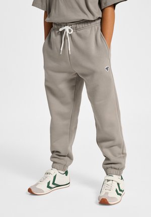 Szare spodnie dresowe z elastycznym pasem i białym sznurkiem, z bocznymi kieszeniami i małym logo na udzie. Połączone z białymi i zielonymi sneakersami.