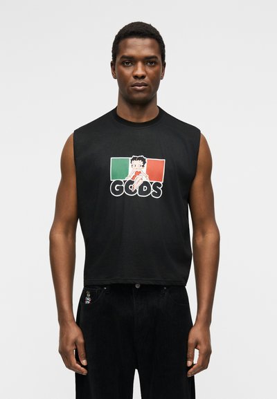 Άνδρας που φοράει μαύρο αμάνικο με χαρακτήρα κινουμένων σχεδίων πάνω από την ιταλική σημαία και το κείμενο «GCDS», σε συνδυασμό με μαύρο παντελόνι.