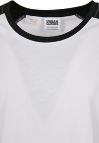 Hvid t-shirt med en sort ribbet rund hals. Har et vaskeetiket og syninger. Fremstillet af blødt bomuldsmateriale.