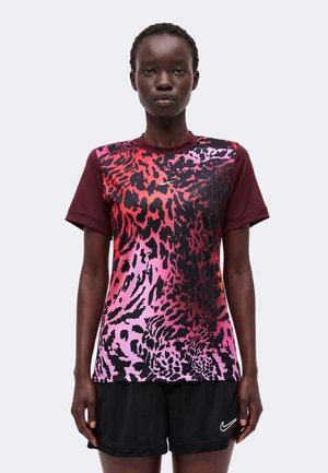Kvinde iført en kortærmet sportstrøje med rød og lyserød leopardprint og sorte shorts med hvid Nike-logo.