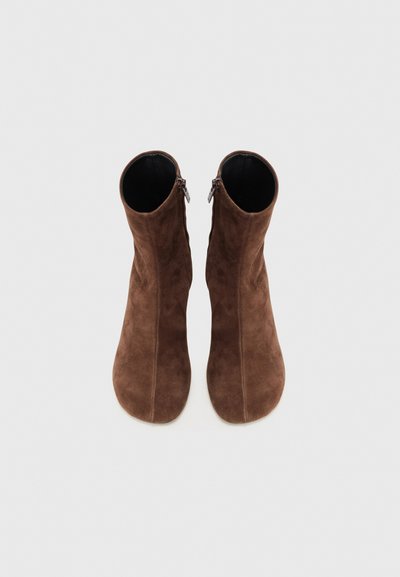 Botas de tobillo de ante marrón con una textura suave, que cuentan con una cremallera lateral y una forma suavemente contorneada, adecuadas para varios estilos.
