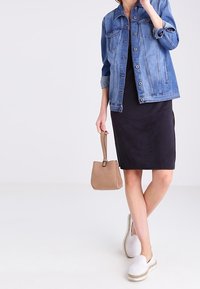 Sininen farkkutakki, jossa napitus, musta mekko, vaaleanruskea laukku ja valkoiset slip-on-kengät, joissa on kudottu pohja.