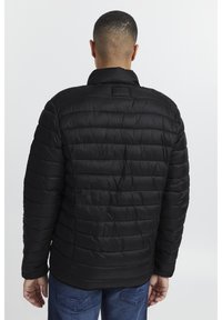 Black insulated jacket with a quilted design. Features a high collar and a smooth texture, shown from the back in a neutral background.