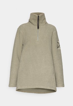 Fleece pullover in light olive green, featuring a high collar, half-zip closure, and textured fabric. Decorated with a geometric patch on the sleeve.