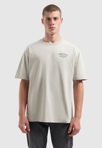 Lichtgrijze t-shirt met korte mouwen van zachte stof, met een klein bedrukt ontwerp op de linkerkant van de borst en een ontspannen, boxy pasvorm.