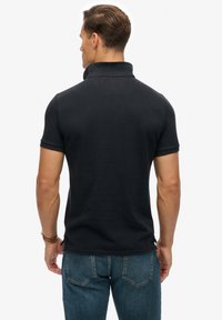 Polo noir avec un col côtelé, des manches courtes et une coupe ajustée. Associez-le à un jean denim bleu foncé avec une légère décoloration.