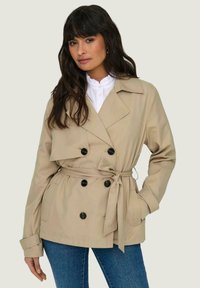 Trench coat beige con design doppiopetto, bottoni neri e vita con cintura. Realizzato in tessuto liscio con vestibilità sartoriale.