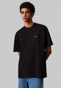 Czarny bawełniany t-shirt z krótkim rękawem i okrągłym dekoltem. Posiada małą łatkę z logo na klatce piersiowej oraz luźny krój.