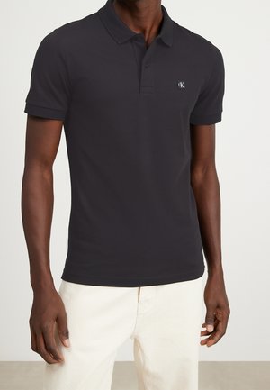 Black polo shirt made of knit fabric, featuring a two-button placket and embroidered logo on the chest. Short sleeves and standard fit.