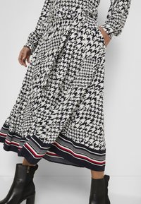 Maxikjol i ett svart och vitt hundtandsmönster, med en kontrasterande randig nederkant med röda accenter och en midja med bälte.