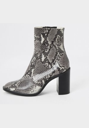 Botte femme hauteur cheville avec motif peau de serpent noir et blanc et talon bloc noir épais sur fond uni.
