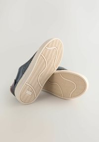 Ādas sporta apavi ar tumši zilu virsu, gaisīgi brūnām akcentiem un baltām gumijas zolēm ar tās teksturētu viļņa rakstu saķerei.