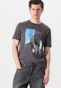 Grå bomulls t-skjorte med grafisk design som viser blå havbilder og tekst. Korte ermer, rund hals, avslappet passform, kombinert med mørke jeans.