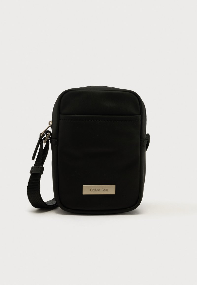 Fekete, texturált nejlon keresztpántos táska, téglalap alakú, elöl cipzáras zsebbel és fémlogóval. Állítható pánttal.