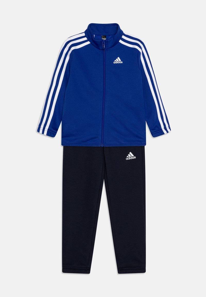 Chandal azul con tres rayas blancas en las mangas. Chaqueta con cremallera que cuenta con un cuello alto. Pantalones marinos a juego con el logo en la parte inferior de la pierna.