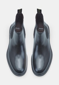 Botas Chelsea de cuero negro con textura suave, paneles laterales elásticos y una tira de agarre a rayas verdes. Punta redonda y suela de goma plana.