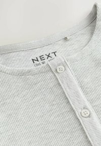 Col à côtes gris avec deux boutons blancs et étiquette imprimée "NEXT LOVE ME" à l'intérieur du col.