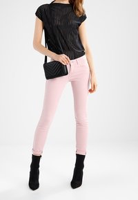 Top corto de manga corta a rayas negras, jeans ajustados rosas, botas negras hasta el tobillo. Pequeña bolsa negra tipo bandolera, que muestra un patrón de chevrón y detalles trenzados.