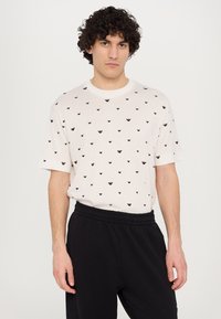 Cream short-sleeve t-shirt featuring a black heart-shaped pattern, paired with black elastic-waist pants. Soft fabric and relaxed fit.