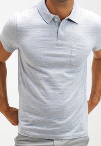 Polo shirt bleu clair à manches courtes en tissu texturé ; comporte un col plié, trois boutons et une poche poitrine.