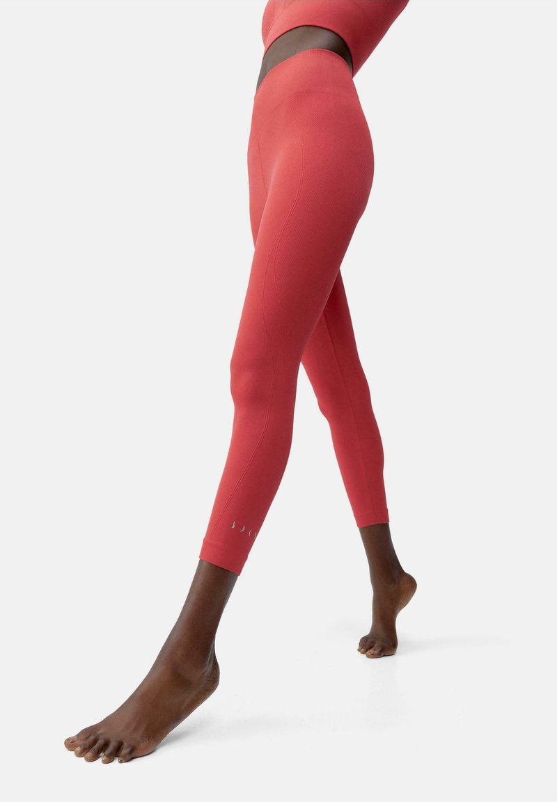 Leggings rossi a vita alta con una finitura testurizzata, caratterizzati da un design aderente, lunghezza alla caviglia e dettagli a taglio discreti sui polsi.