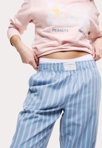 Ljusrosa sweatshirt med vit text och pyjamasbyxor i blå- och rosa ränder. Tyget ser mjukt ut med resårmidja och logodetalj.