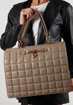 Beige quiltet håndtaske med en glat tekstur, guld kædeaccentuer og et hjerteformet vedhæng, der har dobbelte håndtag til bæring.