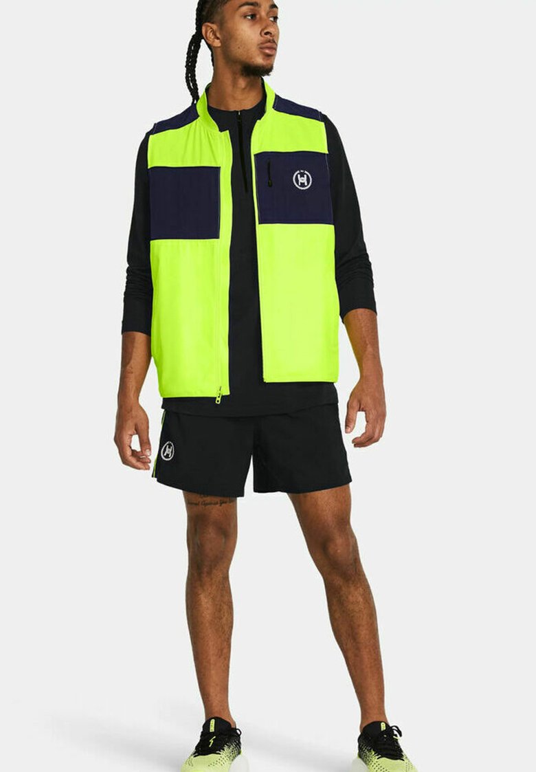 Chaleco de alta visibilidad en amarillo neón con detalles en azul marino, cierre de cremallera y bolsillos, combinado con pantalones cortos negros y zapatillas.