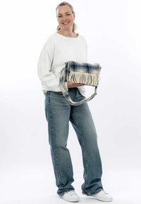 Borsa di denim con dettagli in frange in tonalità di blu e bianco, dotata di tracolla e forma rettangolare. Indossata da un modello in abbigliamento casual.
