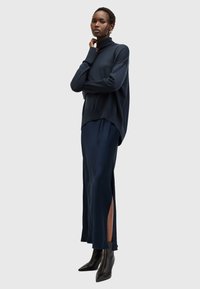 Marineblå strikket turtleneck-genser, oversized passform, kombinert med et langt marineblått skjørt med sidespalter, fullført med svarte ankelstøvler.