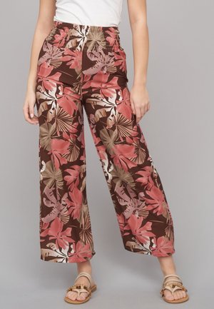 Woman wearing high-waist, wide-leg pants with pink and brown tropical floral pattern, paired with beige beaded sandals and white top.