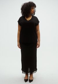 Black, short-sleeve top with a scalloped neckline paired with a black, glittery, long skirt. Model wearing pointed black flats.