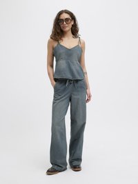Denim kombinacija koja se sastoji od široko krojene bluze s podešivim naramenicama i visokog struka širokih hlača u srednje plavoj boji. Očigledno naglašena detaljima džepova.