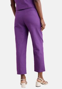 Fioletowe lniane spodnie o prostym kroju, z tylnymi kieszeniami i mankietami długości kostek, zestawione z białymi sandałami na słupku.