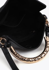 Borsa nera con manico dorato a logo, aperta per rivelare un interno nero con una tasca con zip. Il design è elegante e moderno.