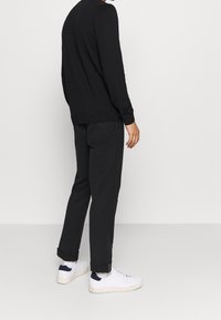 Schwarzer Pullover und Hose mit lockerem Schnitt, kombiniert mit weißen Turnschuhen mit marineblauen Akzenten. Strickstruktur auf dem Pullover sichtbar.