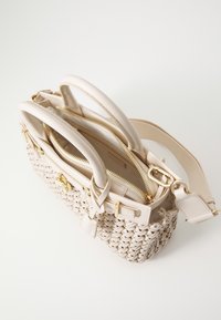 Sac à main tissé beige avec deux poignées, une fermeture éclair dorée et une bandoulière amovible sur fond blanc.