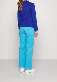 Chaqueta azul con diseño estructurado, combinada con pantalones de pana de pierna ancha en azul claro. Footwear blanco completa el conjunto.