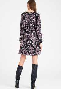 Robe fleurie avec un fond noir, ornée de motifs floraux violets et blancs, à manches bouffantes longues et à ourlet  évasé. Portée avec des bottes noires montantes.