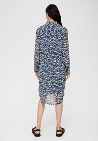 Robe longue semi-transparente présentant un motif abstrait bleu et crème, à manches longues et col, avec un ourlet légèrement arrondi.