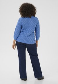 Lyseblå strikket sweater med struktureret mønster, trekvartærmer og ribbet kant, sammen med mørke denimbukser og sorte sko.