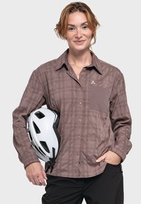 Brown plaid long-sleeve shirt with a button-down design, chest pocket, and a logo; held with a white and black bicycle helmet.