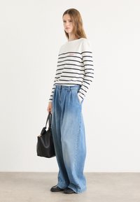 Gestreept langetermijnshirt in wit en marineblauw, gecombineerd met losse lichtblauwe denim broek. Een zwarte totebag en donkere schoenen maken de look compleet.