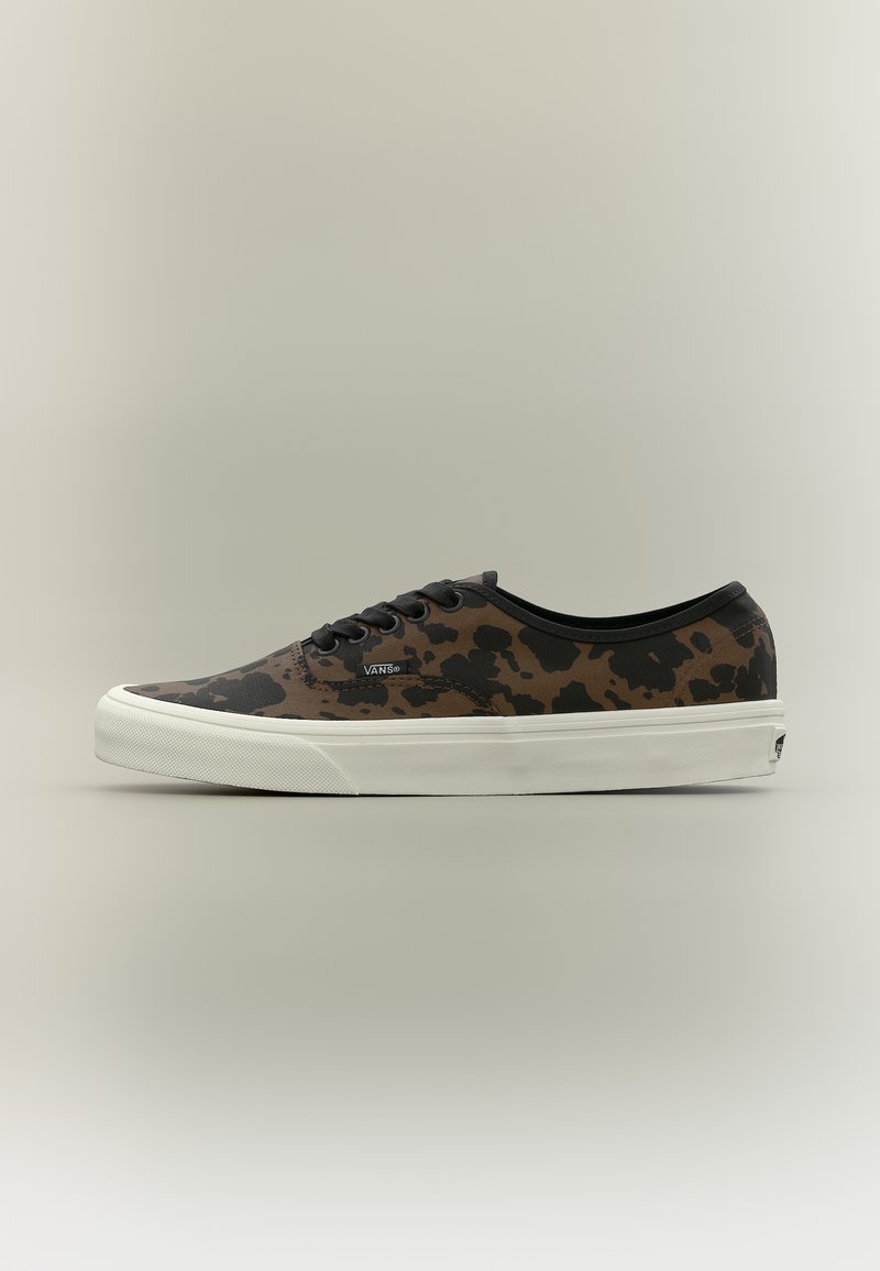 Baskets basses Vans avec un motif camouflage marron et noir, lacets noirs, et semelle en caoutchouc blanche sur un fond neutre.