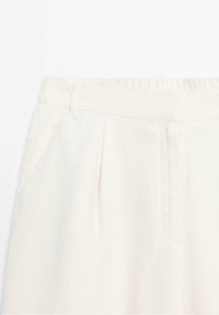Pantalons en lin rose clair avec une taille élastique, des plis à l'avant et des poches latérales, montrant un tissu doux et texturé.